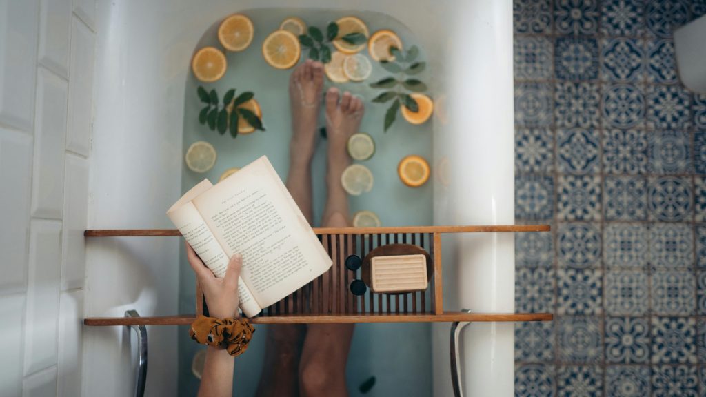 Personne lisant un livre dans un bain relaxant avec agrumes et plantes - bien-être par la bibliothérapie