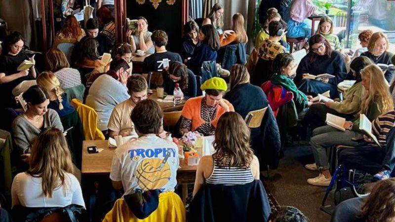 Groupe de personnes lisant silencieusement ensemble dans un café animé, lors d'une Silent Reading Party